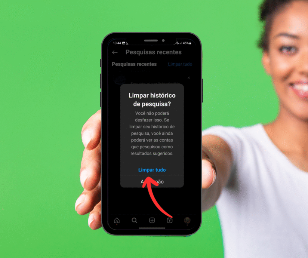 Uma imagem de uma mulher segurando um smartphone com o aplicativo do Instagram aberto. A tela exibe um pop-up de confirmação com a mensagem "Limpar histórico de pesquisa?", explicando que a ação não pode ser desfeita. A seta vermelha curva aponta para a opção "Limpar tudo" no pop-up, indicando o último passo para o usuário confirmar e apagar sugestões e o histórico de pesquisa.
