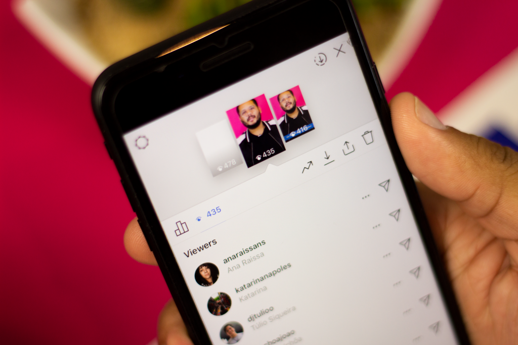 Close-up de uma mão segurando um smartphone com a tela exibindo a área de estatísticas de um Story (provavelmente Instagram), mostrando o número de visualizações (435) e a lista de espectadores ('Viewers'), que inclui nomes de usuários. A imagem é um foco direto na análise das métricas de desempenho e do alcance dos stories em uma plataforma social.
