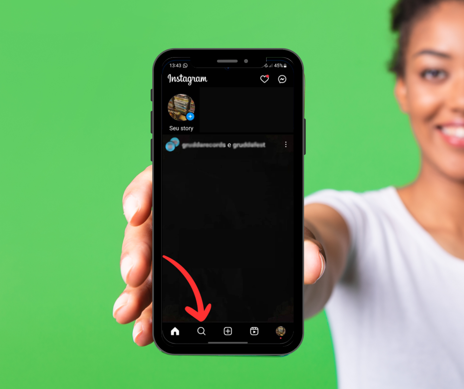 Uma imagem de uma mulher segurando um smartphone com o aplicativo do Instagram aberto. A tela exibe a página inicial do aplicativo e uma seta vermelha curvada aponta para a barra de navegação inferior. O ícone de pesquisa (uma lupa) está destacado no centro da barra, indicando o local onde o usuário pode encontrar e apagar sugestões de contas, reels e outros conteúdos.